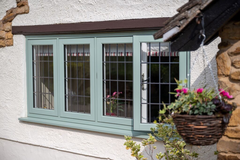 A flush sash window featuring a green frame and brown trim, showcasing clear glass panes.